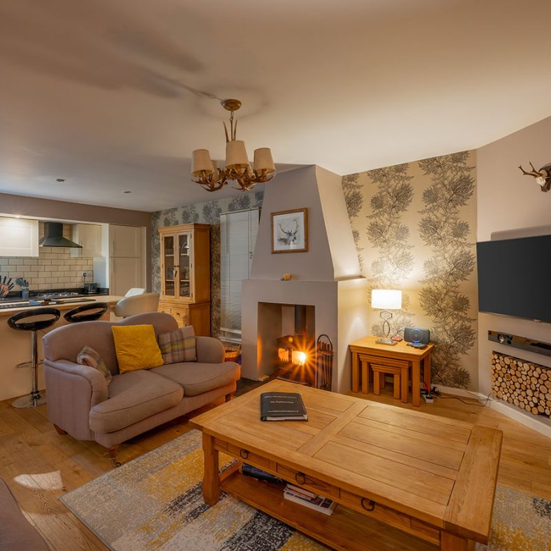 The living room and kitchen and a wood burning stove in Courtyard Cottage 11 at Abbey Holidays Loch Ness