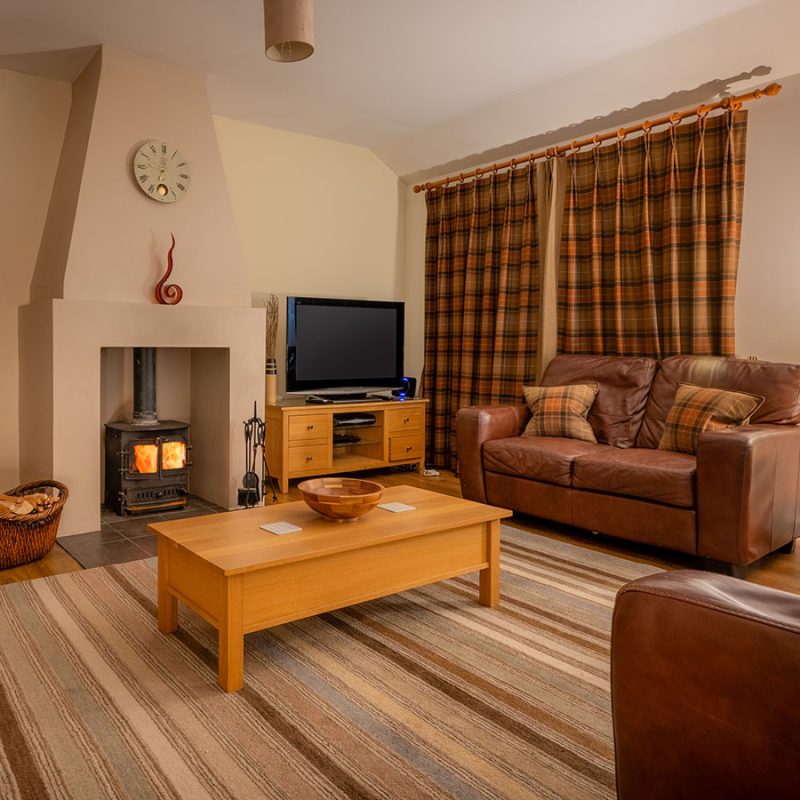 The cosy living room with a log burner lit in the Club Cottage accommodation at Abbey Holidays Loch Ness