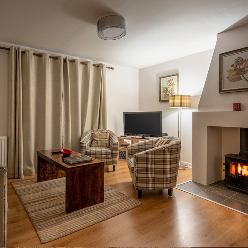 The cosy living room with lit log burner in the Brora accommodation at Abbey Holidays Loch Ness