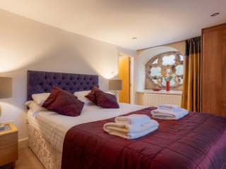 Moat House 5 The Ross accommodation&#039;s double bedroom with beautiful circular stained glass window at Abbey Holidays Loch Ness