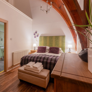 The Caledonian - Old School 12 accommodation&#039;s double bedroom with stunning arched beams and en-suite at Abbey Holidays Loch Ness